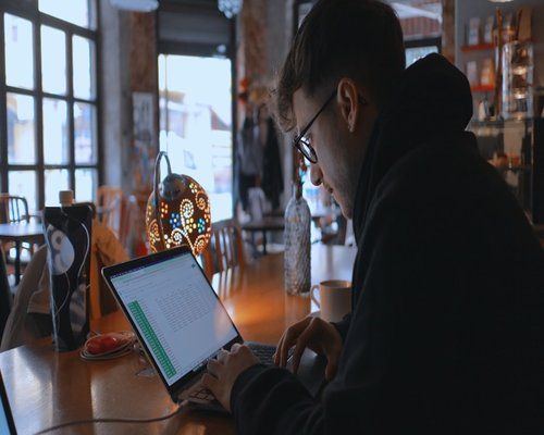 Man typing an email on a laptop in a cafe